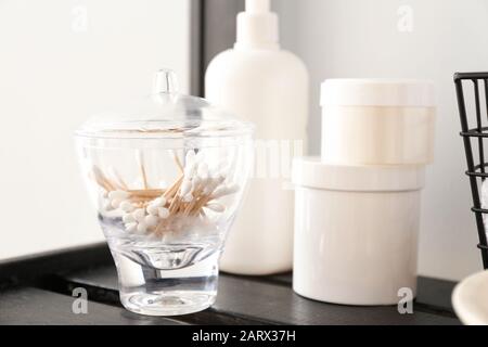 Cotton swabs with body care cosmetics on shelf in bathroom Stock Photo