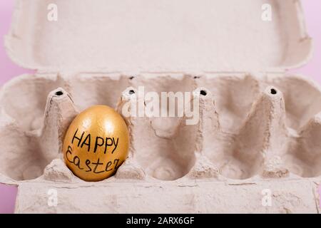 Single golden chicken egg in an open carton box with Happy Easter message Stock Photo