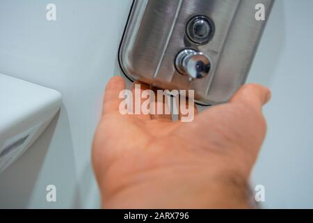 Close-up of male hand trying to get soap from liquid soap dispenser on wall Stock Photo