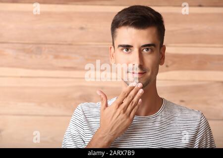 Young deaf mute man using sign language on wooden background Stock Photo