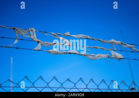A barbed wire fence with tattered material tangled in it Stock Photo