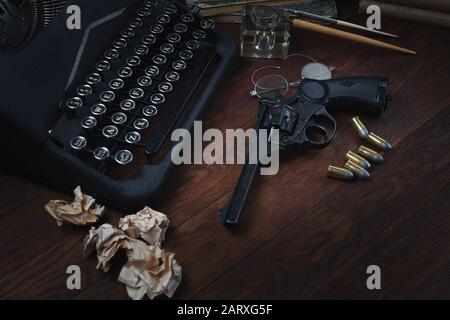 Crime fiction story - old retro vintage typewriter and revolver gun with ammunitions, books, blank paper, old ink pen on wooden table