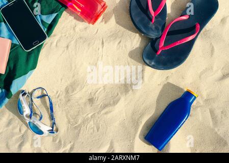 vacation and summer holidays concept - flip flops, towel, cap, bottled water and bottle of sunscreen oil on beach sand Stock Photo