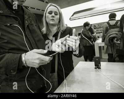 Paris, France - Nov 3, 2017: Side view of young couple admiring inside Apple Store the latest professional iPhone smartphone manufactured by Apple Computers comparing with older model Android phone - black and white Stock Photo