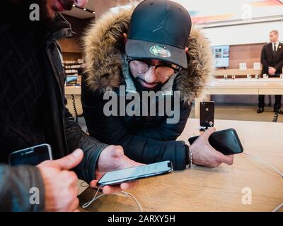 Paris, France - Nov 3, 2017: Male friends customers admiring inside Apple Store the latest professional iPhone smartphone manufactured by Apple Computers Stock Photo