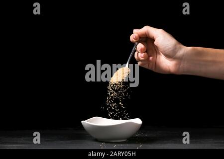 Woman pouring sugar from spoon into bowl on dark background Stock Photo