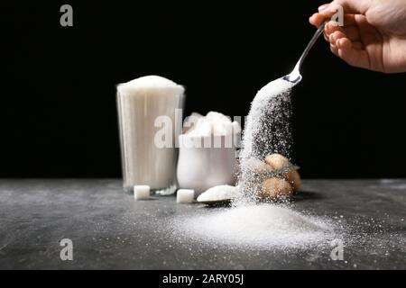 Woman pouring sugar from spoon onto table Stock Photo