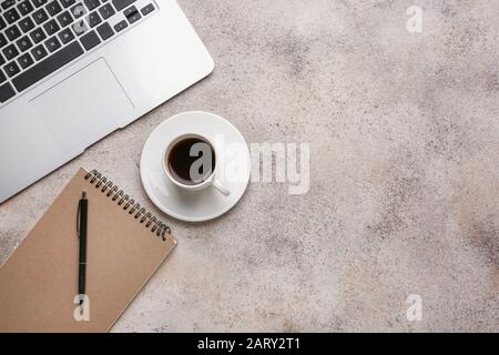 Cup of hot coffee with laptop and stationery on grey background Stock Photo