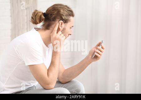 Young man with hearing aid using mobile phone at home Stock Photo