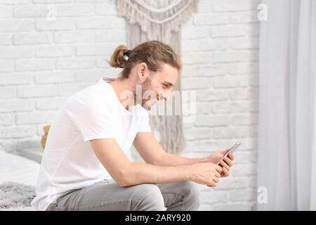 Young man with hearing aid using mobile phone at home Stock Photo