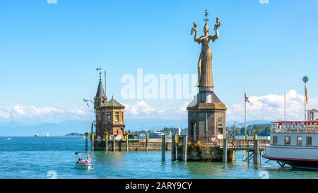 Constance, Germany – July 30, 2019: Old lighthouse and big statue of Imperia in harbor of Konstanz, Germany. Imperia is a landmark of the city. Panora Stock Photo