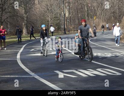 Family of four ride bikes on the road in Prospect Park, Brooklyn, New York. Stock Photo