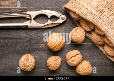 Sack with tasty walnuts and nutcracker on wooden background Stock Photo