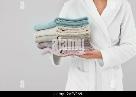Woman holding stack of towels on light background Stock Photo