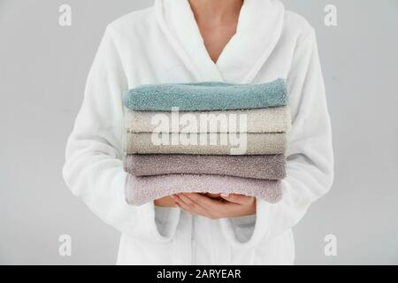 Woman holding stack of towels on light background Stock Photo