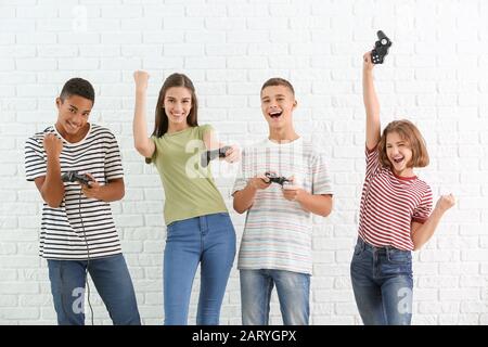 Happy teenagers playing video games against white brick background Stock Photo