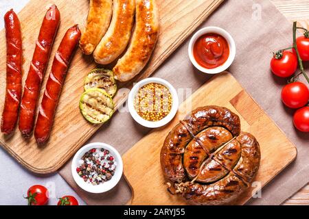 Wooden boards with tasty grilled sausages and sauces on table Stock Photo