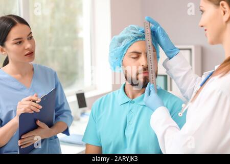 Plastic surgeon examining young man's face prior to operation in clinic Stock Photo