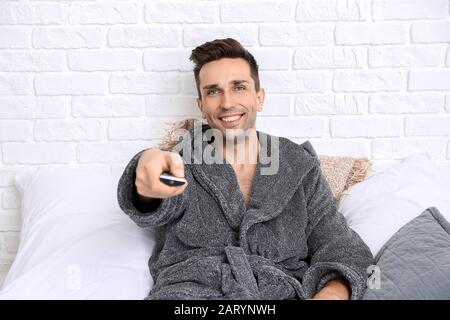 Handsome man in bathrobe watching TV on bed Stock Photo