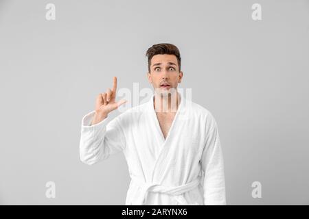 Surprised man in bathrobe pointing at something on grey background Stock Photo
