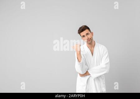 Handsome man in bathrobe pointing at something on grey background Stock Photo