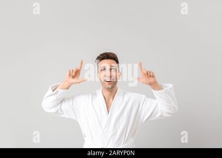 Handsome man in bathrobe pointing at something on grey background Stock Photo