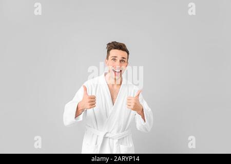 Happy man in bathrobe showing thumb-up gesture on grey background Stock Photo