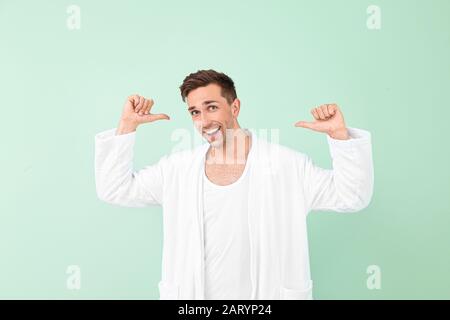 Happy man in bathrobe showing something on color background Stock Photo