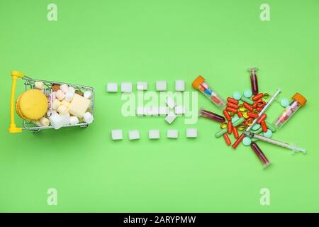 Composition with sweets in shopping cart and medicines on color background Stock Photo