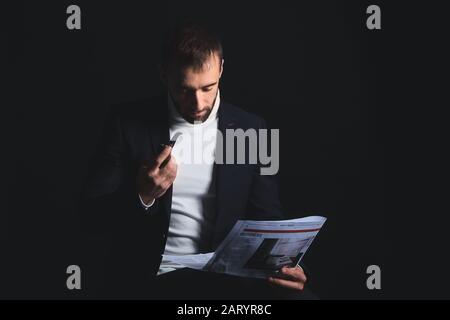 Portrait of stylish young man with newspaper and smoking pipe on dark background Stock Photo