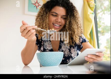 Smiling woman using tablet while eating breakfast Stock Photo