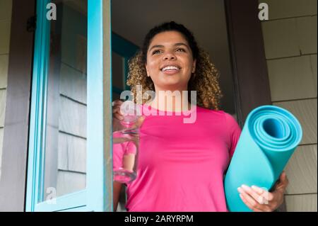 Smiling woman holding drink bottle and yoga mat Stock Photo