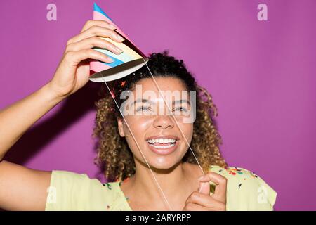 Smiling woman putting on party hat Stock Photo