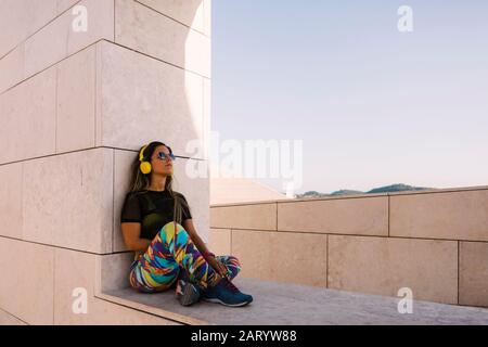 Woman wearing headphones sitting on wall Stock Photo