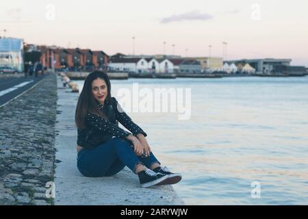 Woman sitting on footpath by sea in Lisbon, Portugal Stock Photo