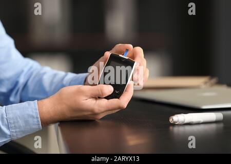 Diabetic man checking blood sugar level in office, closeup Stock Photo