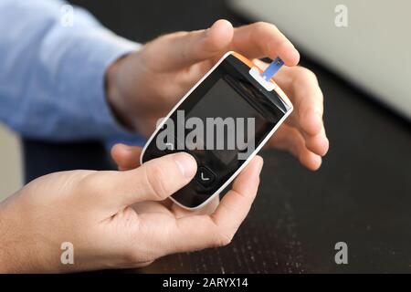 Diabetic man checking blood sugar level in office, closeup Stock Photo