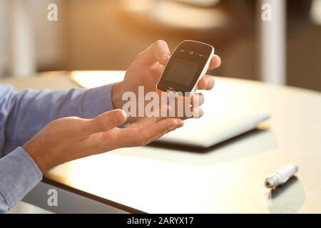 Diabetic man checking blood sugar level in office, closeup Stock Photo