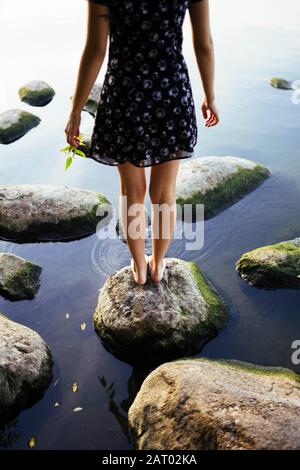 Barefoot woman standing on rock in sea Stock Photo