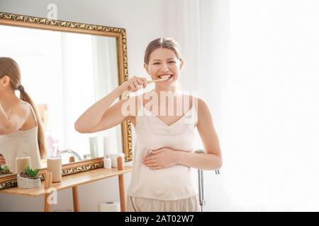 Young pregnant woman brushing teeth in bathroom Stock Photo