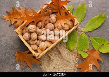 Box with tasty walnuts and autumn leaves on grey background Stock Photo