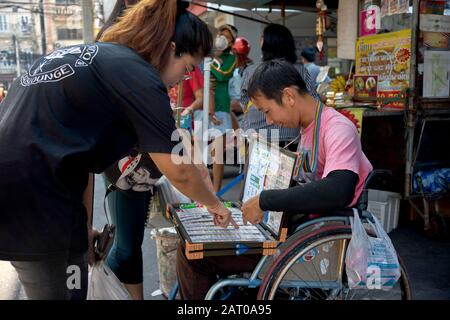Disabled man in a wheelchair working and selling lottery tickets on a Thailand street Stock Photo
