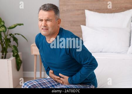 Mature man suffering from abdominal pain in bedroom Stock Photo