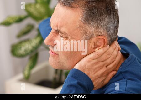 Mature man suffering from neck pain in bedroom Stock Photo