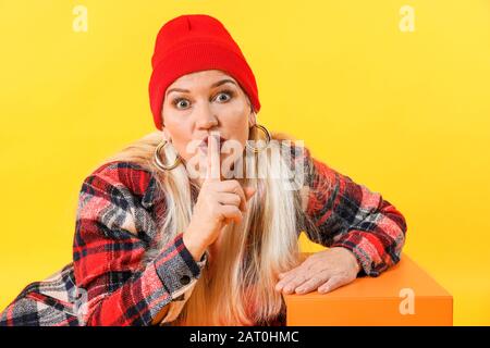 Fashionable mature woman showing silence gesture on color background Stock Photo