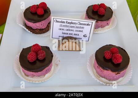 Chocolate raspberry cheesecake at a homemade food stand at the local farmer's market. Glossy frosting with three berries on top. Sign with ingredients Stock Photo