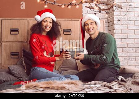 Happy African-American couple with Christmas gift at home Stock Photo