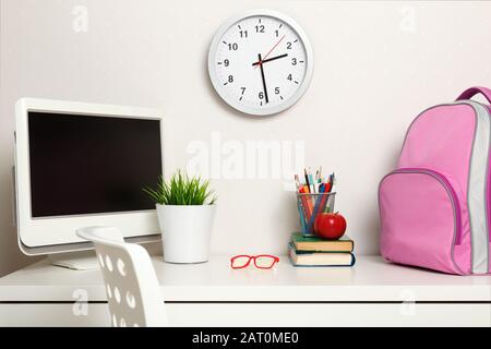 Workplace schoolgirl on the background light walls. On the table books backpack computer stationery glasses. Stock Photo