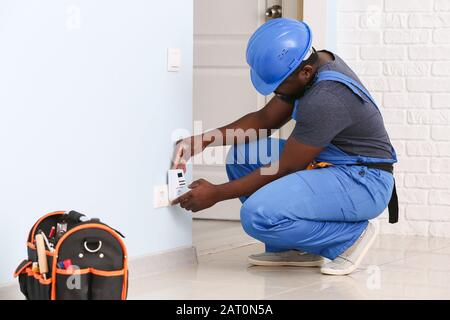 African-American electrician using socket voltage regulator in room Stock Photo