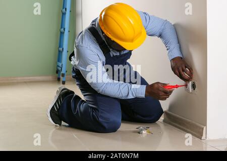 African-American electrician replacing socket in room Stock Photo